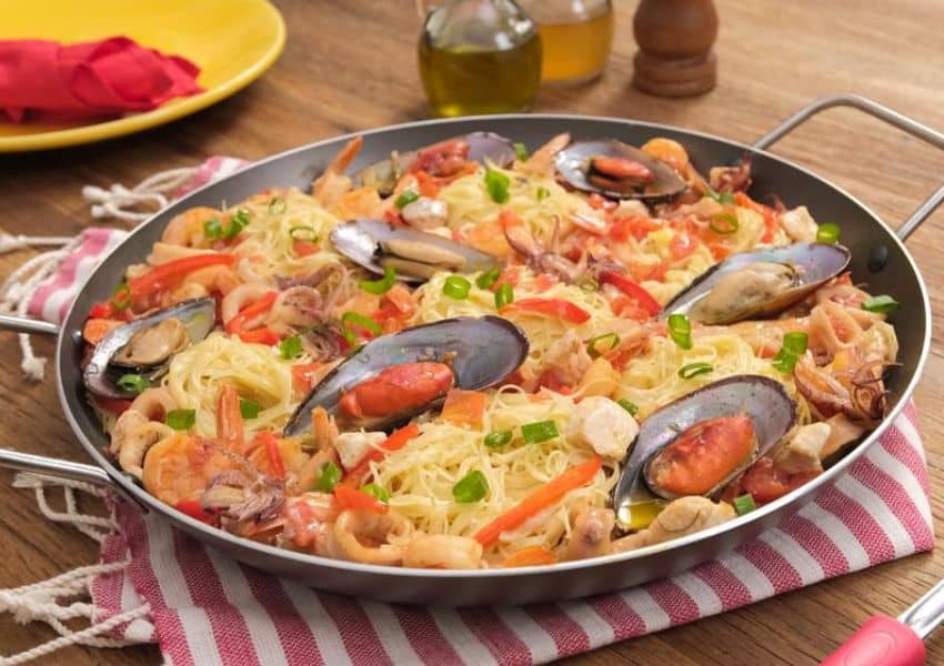 uma panela cheia de macarrão e frutos do mar em cima de uma mesa de madeira.