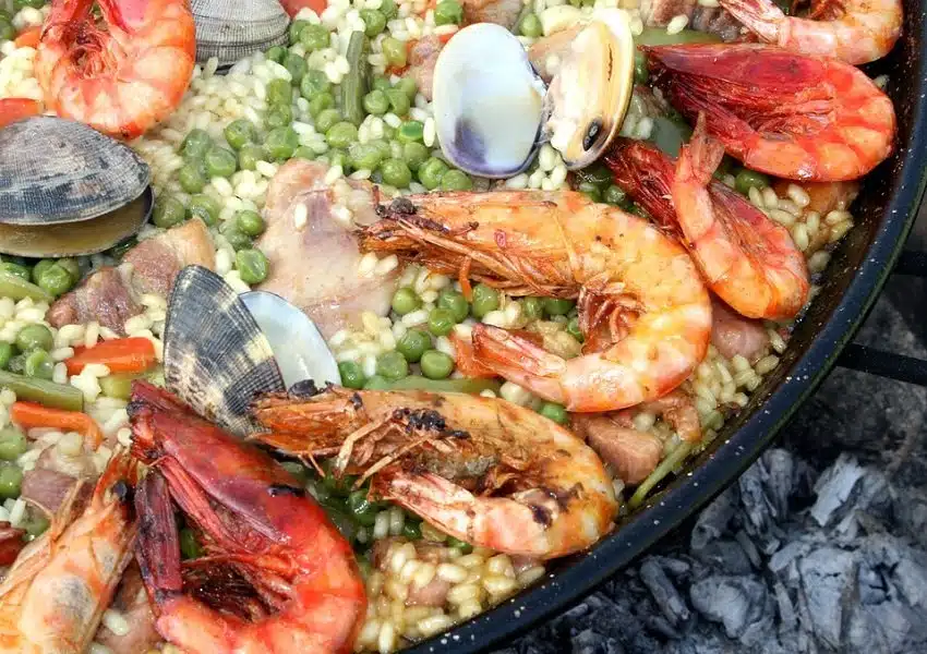 Paella com frutos do mar servida em paelleira tradicional, com camarões, lula, polvo e pimentões coloridos