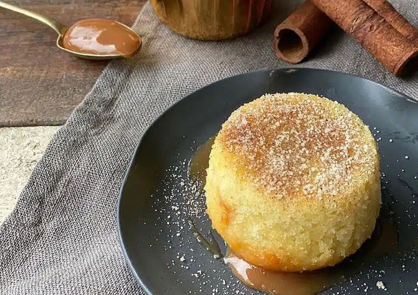 Mini bolinho de churros recheado com doce de leite, polvilhado com açúcar e canela, servido em forminha de muffin