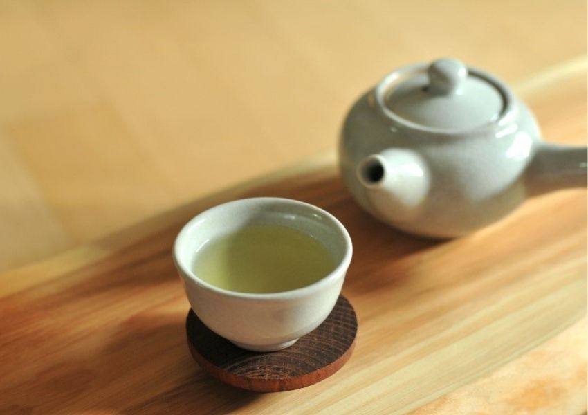 Uma chaleira e uma xícara de chá bem quente sobre uma mesa de madeira clara