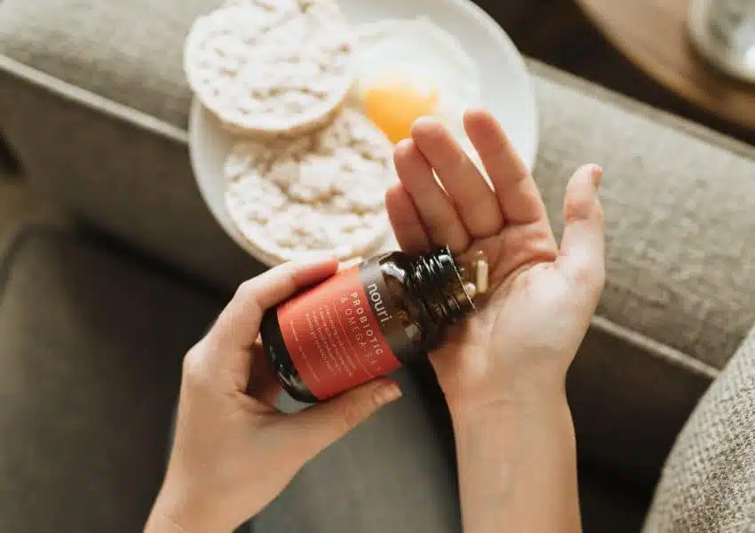Potes de suplementos nutricionais sobre mesa com frutas e vegetais ao fundo