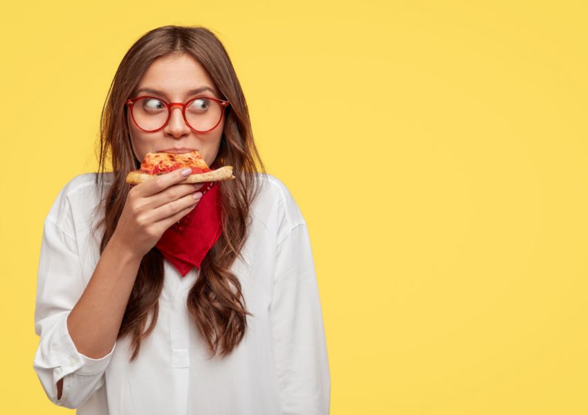 mulher branca comendo pizza com carinha de serelepe - Dicas de alimentação saudável
