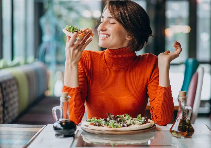 mulher jovem comendo uma pizza pouco sódio com felicidade