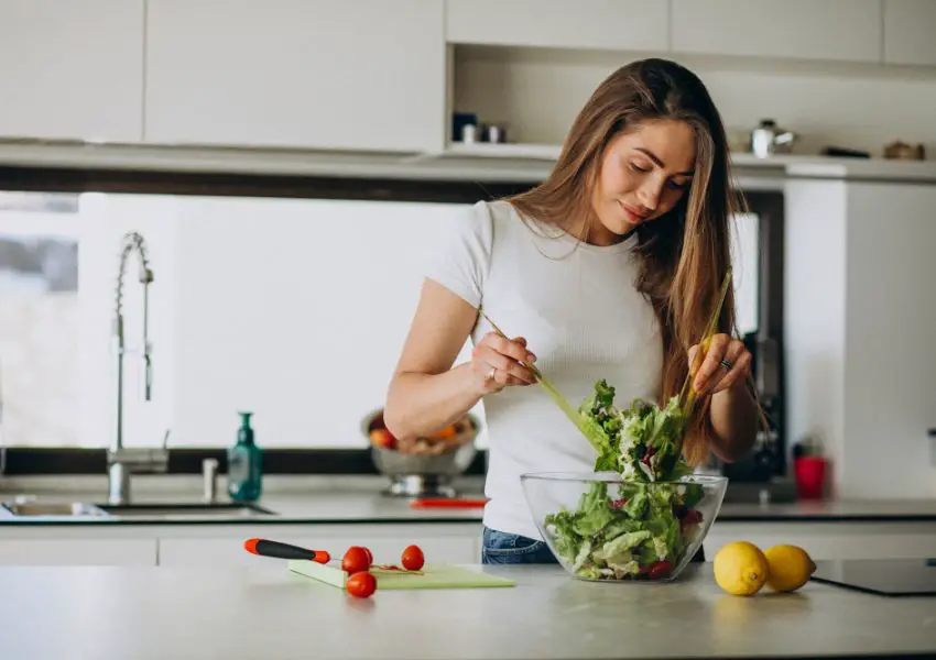 Mulher de camiseta branca preparando uma salada verde