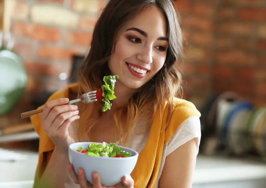 Mulher sorrindo enquanto come uma salada verde com tomates
