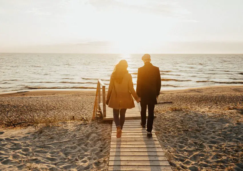 Foto de casal caminhando em direcao ao mar de maos dadas