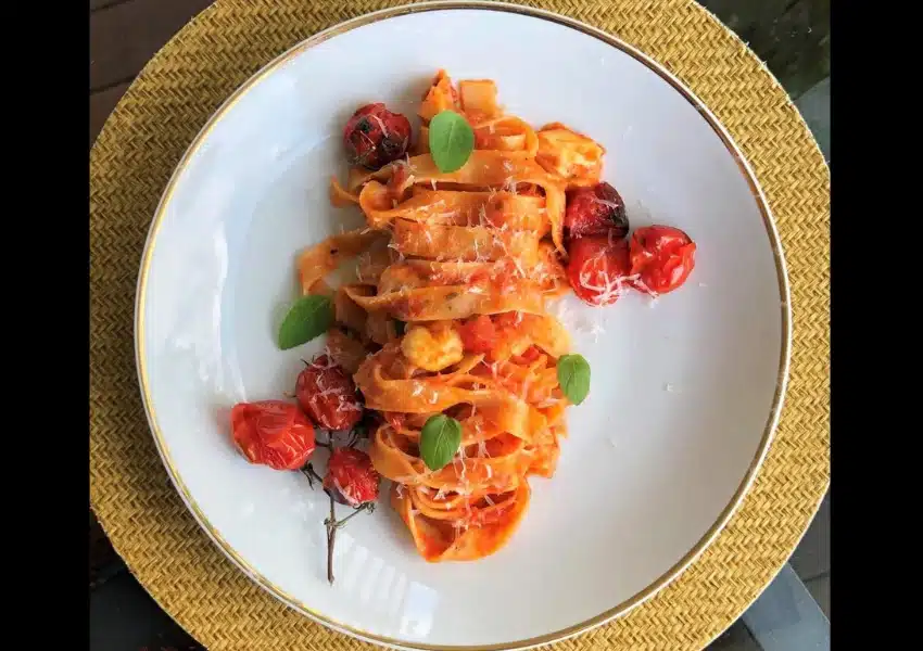 Inicial 1 Prato de Fettuccine à Caprese com molho de tomate, muçarela de búfala e folhas de manjericão fresco, servido em uma panela rústica.